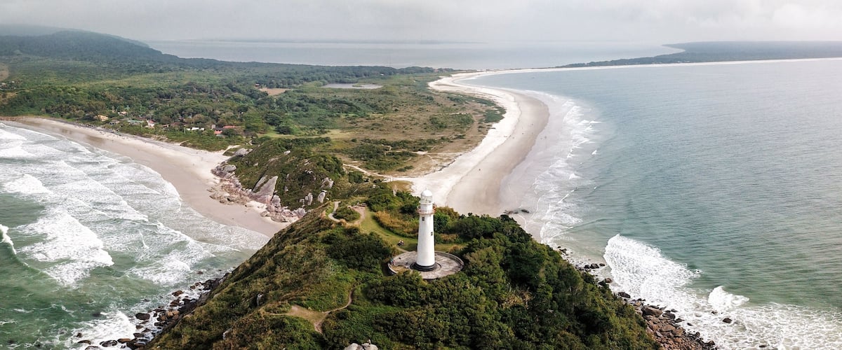 A coastal landscape with a lighthouse, beach, and surrounding greenery.