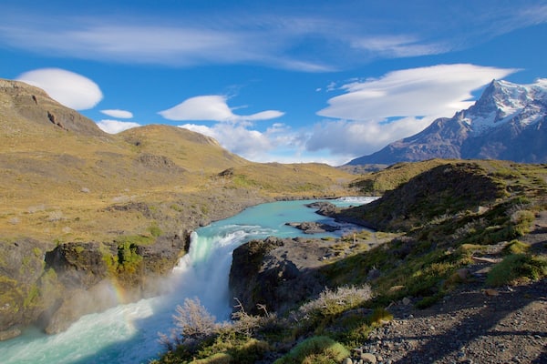 Une cascade se jetant dans un bassin turquoise, entouré de montagnes escarpées et sous un ciel dégagé.