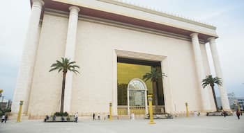A large building with a golden arch entrance, palm trees, and people walking around.