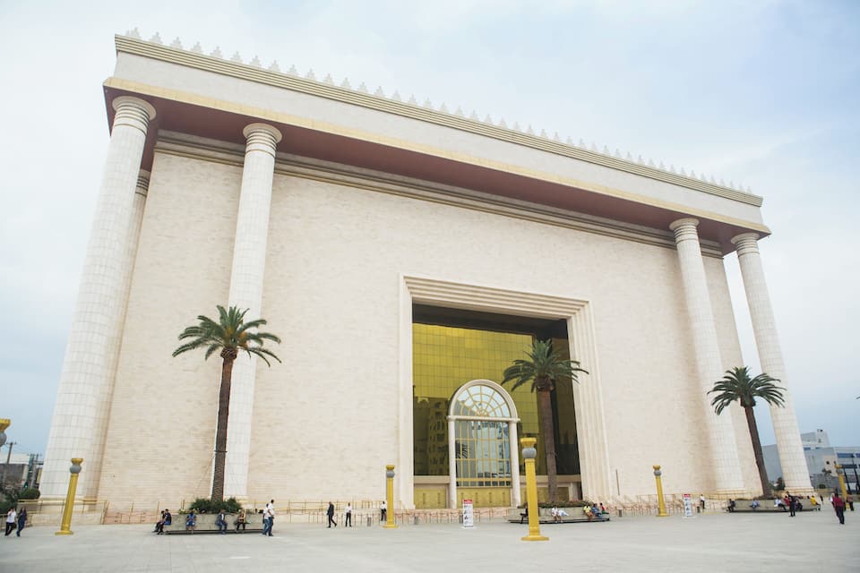 Un grande edificio con un ingresso ad arco dorato, palme e persone che passeggiano.