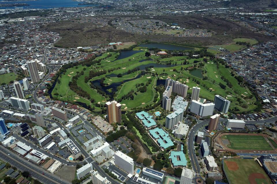 An aerial view of a city with a large park, golf courses, and surrounding residential areas.