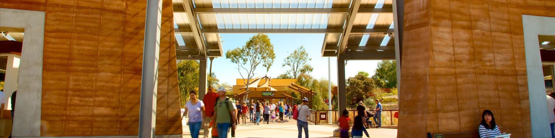 The Phoenix Zoo entrance with a large sign, people walking, and a woman sitting on a bench.