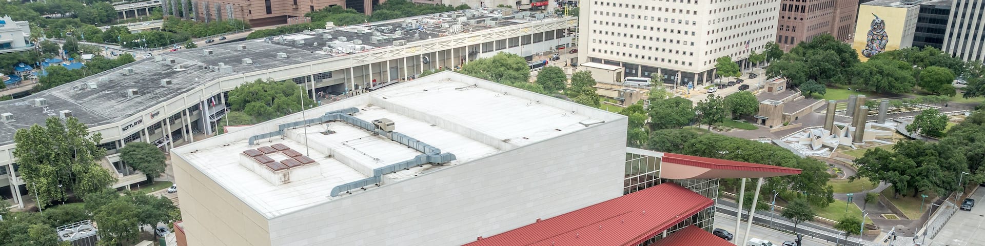 A large building with a red roof and a white facade, surrounded by trees and other buildings.