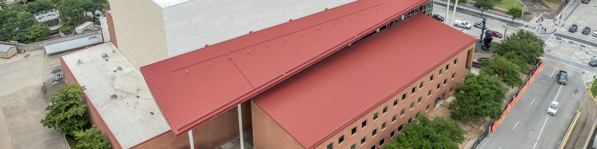 Un grand bâtiment à toit rouge et à façade blanche, entouré d’arbres et d’autres immeubles.