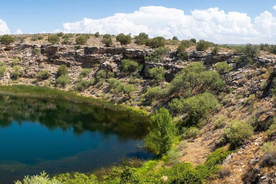 A clear blue lake surrounded by rocky cliffs and sparse vegetation.