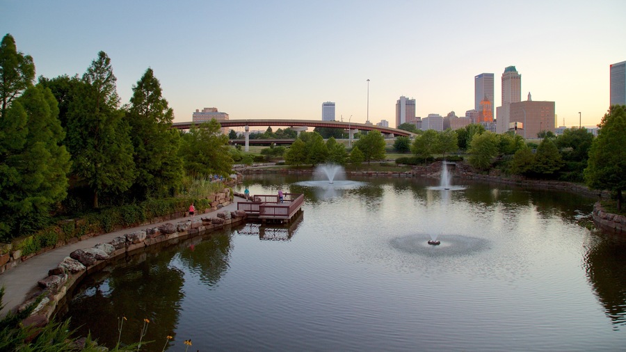 A park with a pond, a wooden deck, and a bridge in the background.