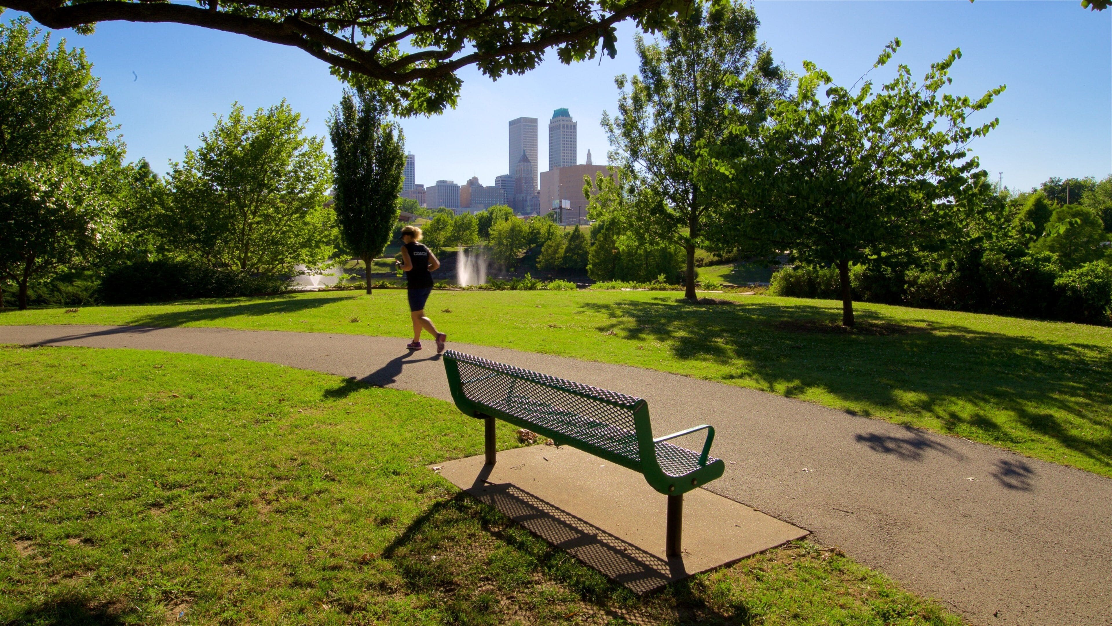 Un parc avec une piste de course, un banc vert et, en arrière-plan, la silhouette de la ville.