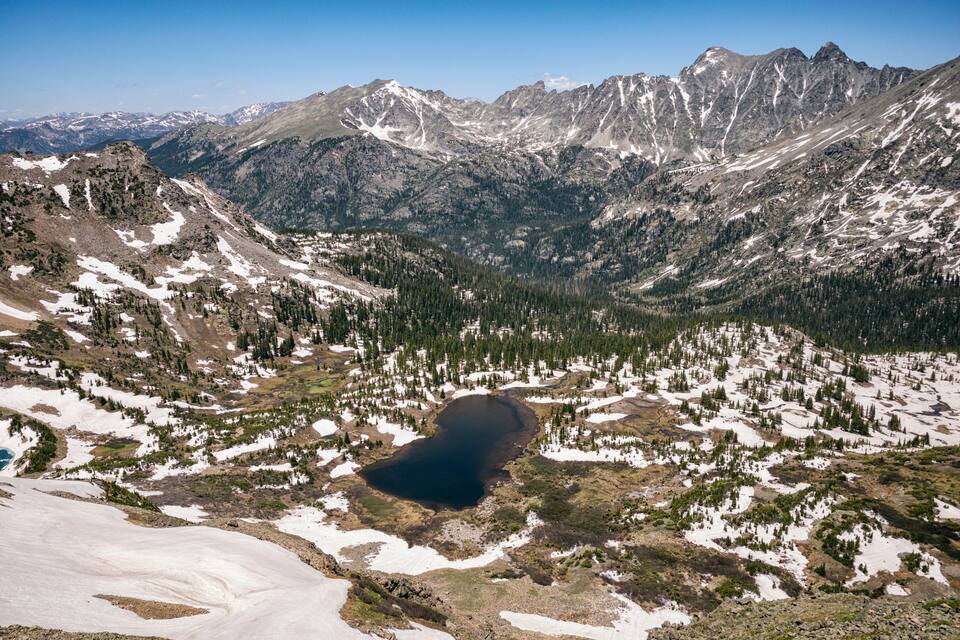Paisatge de muntanya amb un llac envoltat de cims nevats i boscos densos.