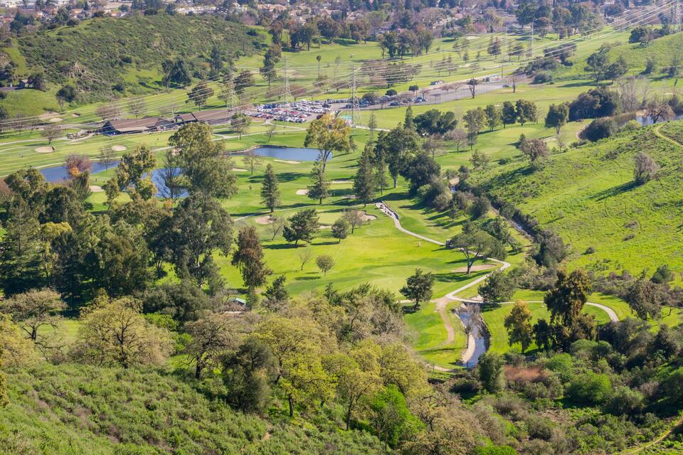 Ein Golfplatz mit Teich, Bäumen und einem Parkplatz.