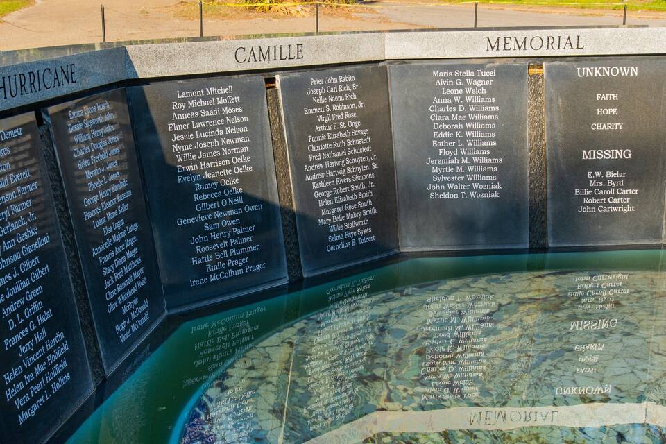 Un mur commemoratiu amb noms i categories com Huracà, Camille, Memorial, Desconegut, Fe, Esperança, Caritat i Desaparegut.