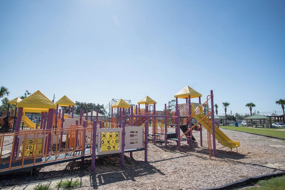 A playground with yellow and purple play structures, including slides and climbing areas.