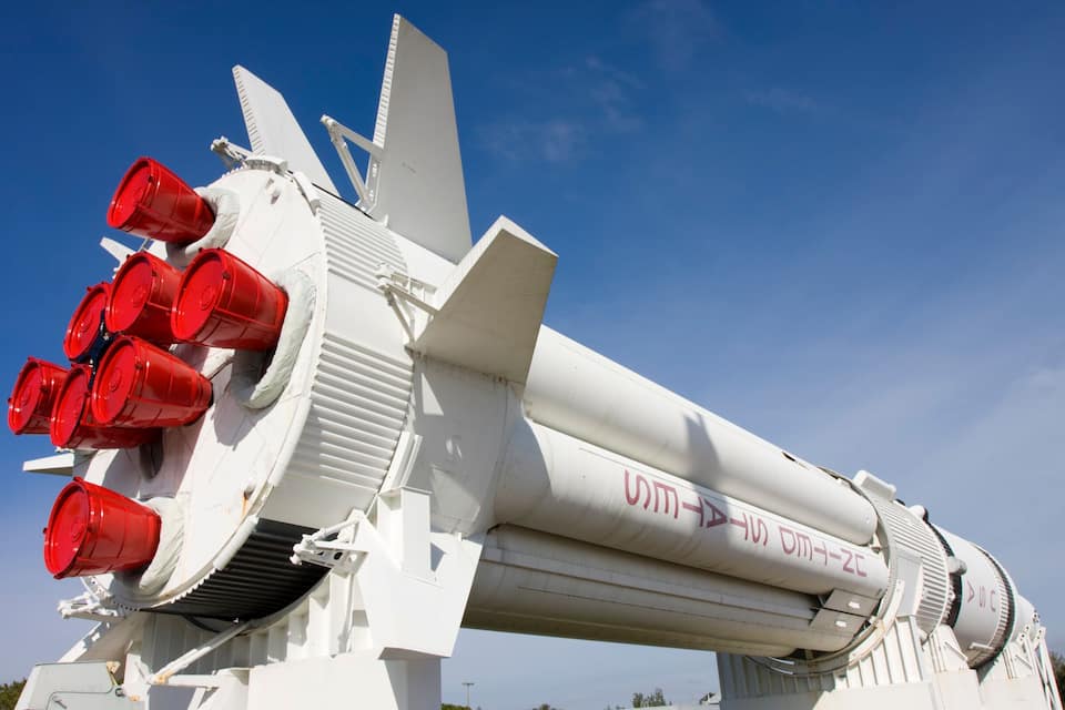 A rocket with multiple red engines and a white body, featuring the text "UMT-1" and "UMT-2" on its side.