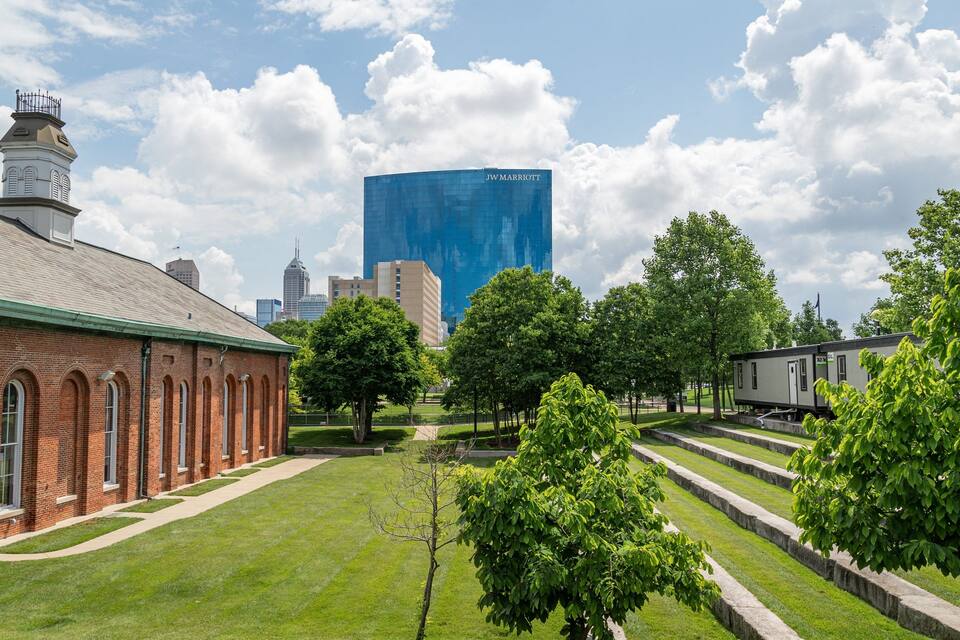 A brick building with arched windows, a grassy lawn, trees, and a modern skyscraper in the background.