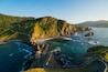 A coastal landscape with a winding road, rocky cliffs, and a clear blue sea.