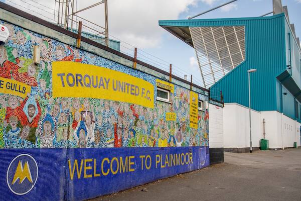Un mur décoré d’une mosaïque colorée sur lequel on peut lire les inscriptions « TORQUAY UNITED FC » et « BIENVENUE À PLAINMOOR ».