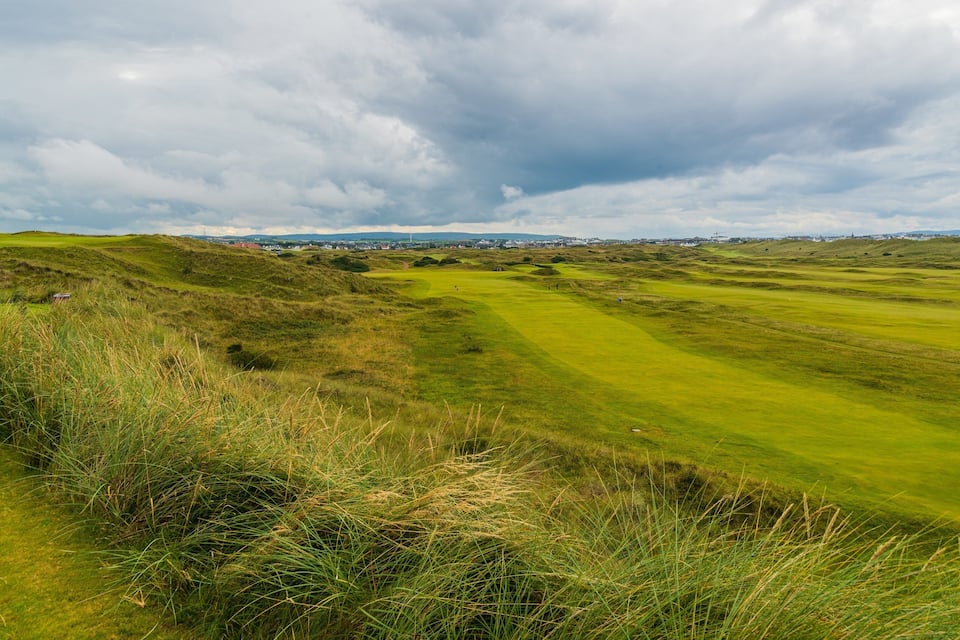 A golf course with rolling hills and a cloudy sky.