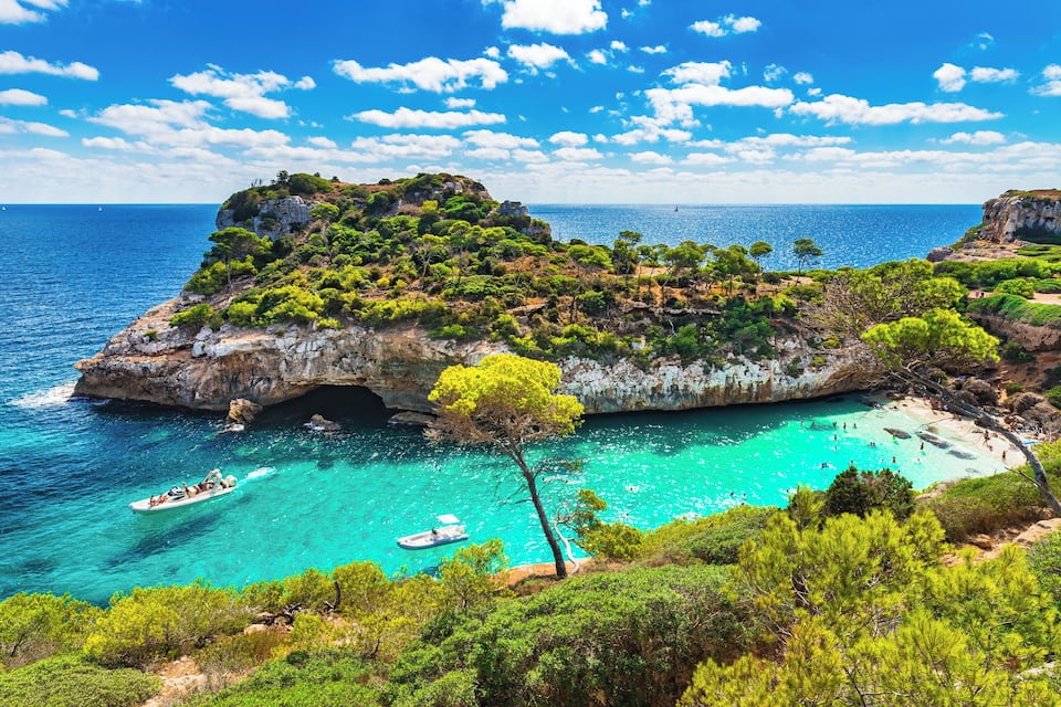 Un paysage côtier avec une île rocheuse, des eaux turquoise et des bateaux.