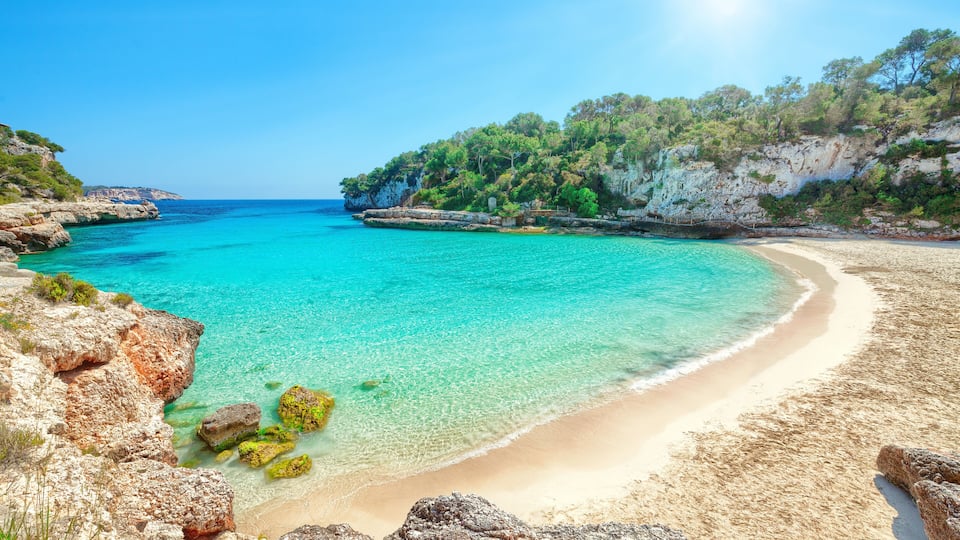 A turquoise beach with clear waters, rocky cliffs, and lush greenery.