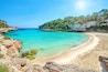 A turquoise beach with clear waters, rocky cliffs, and lush greenery.