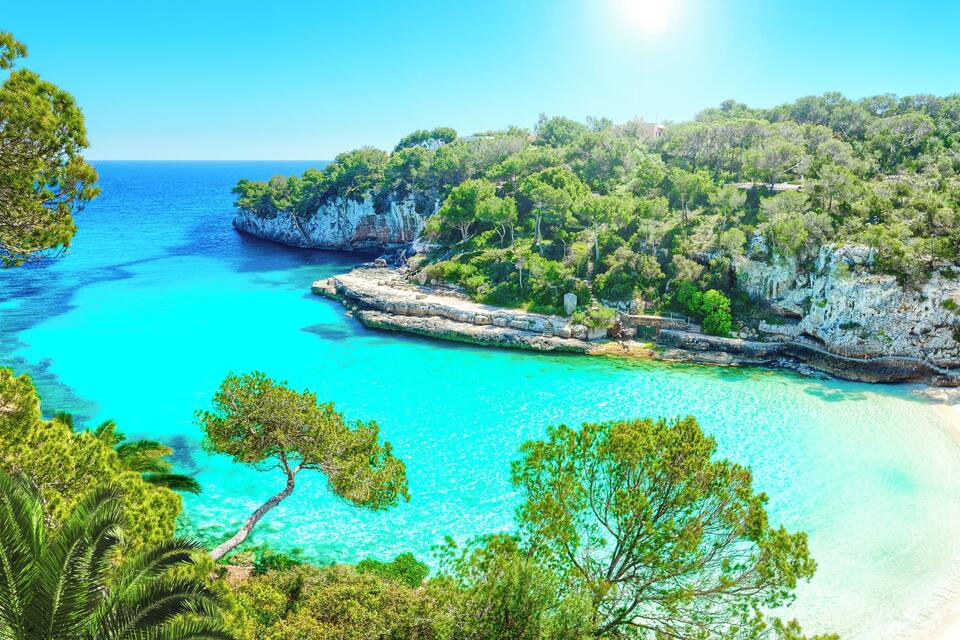 A coastal landscape with turquoise waters, rocky cliffs, and dense greenery.