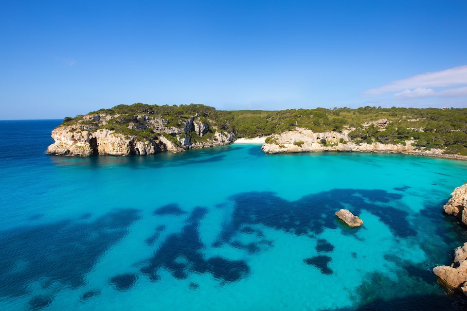 A coastal landscape with clear turquoise waters, rocky cliffs, and lush greenery.