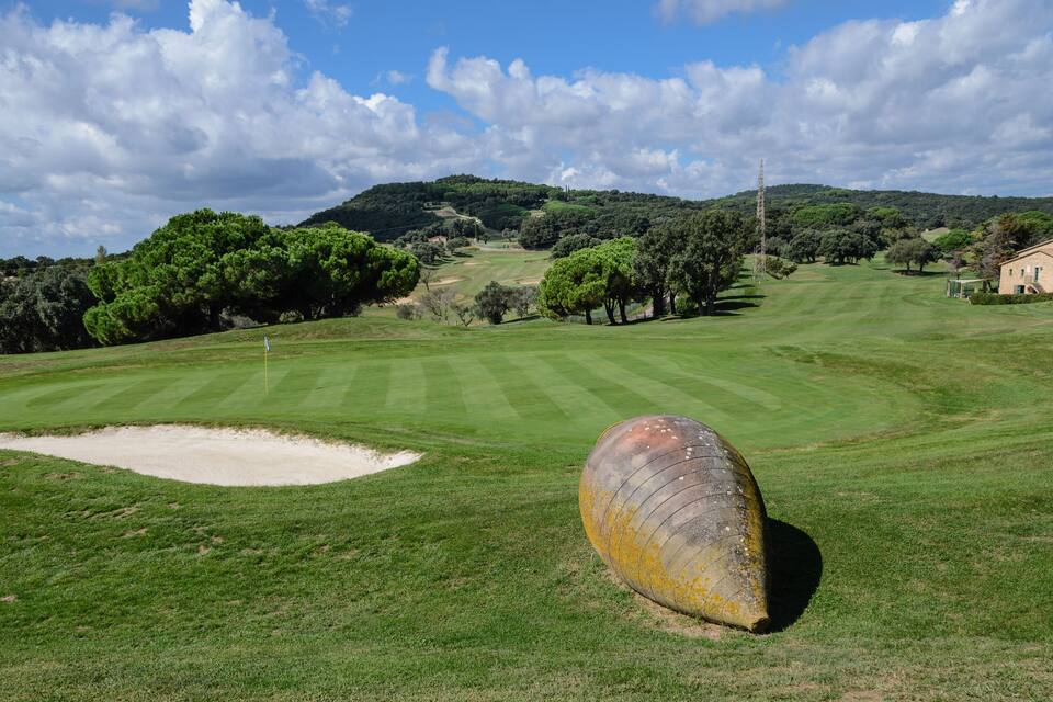 A golf course with a sand bunker, trees, and a stone building in the background.