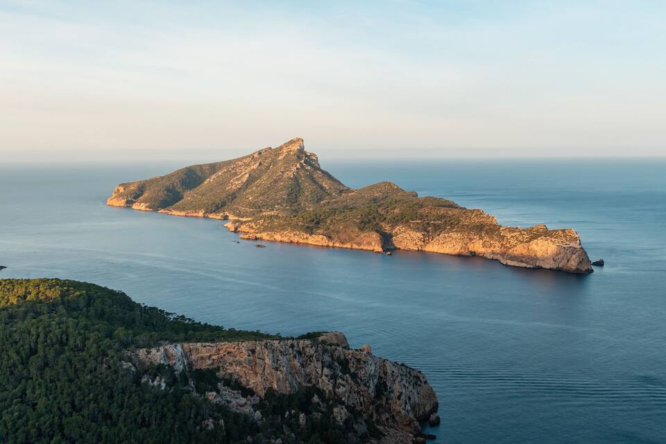 Een ruig eiland met een markante bergtop, omgeven door rustig zeewater en een beboste kustlijn.