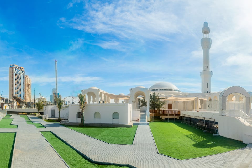 A mosque with a minaret, a Ferris wheel, and modern buildings in the background.