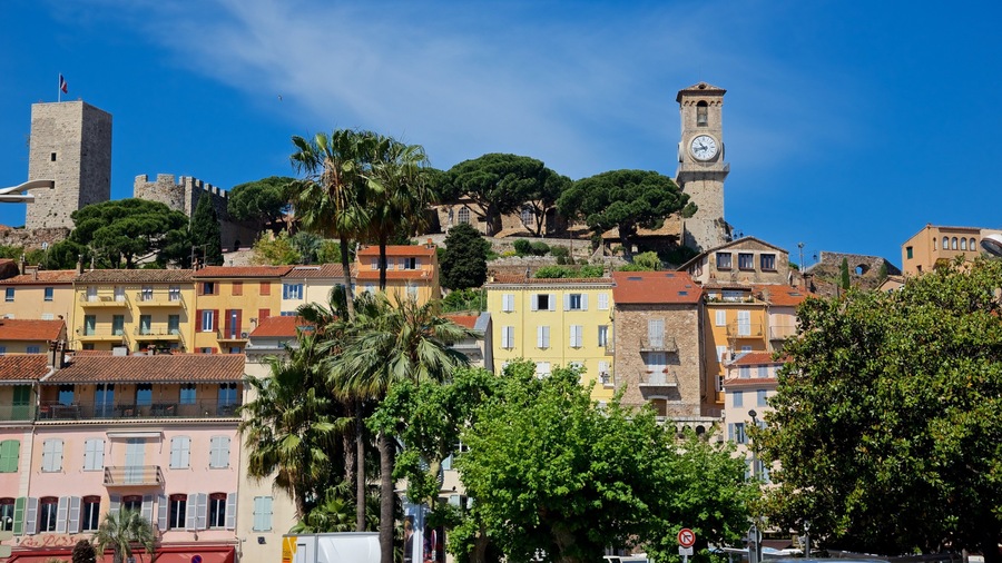 A historic town with colorful buildings, a prominent clock tower, and a castle on a hill.