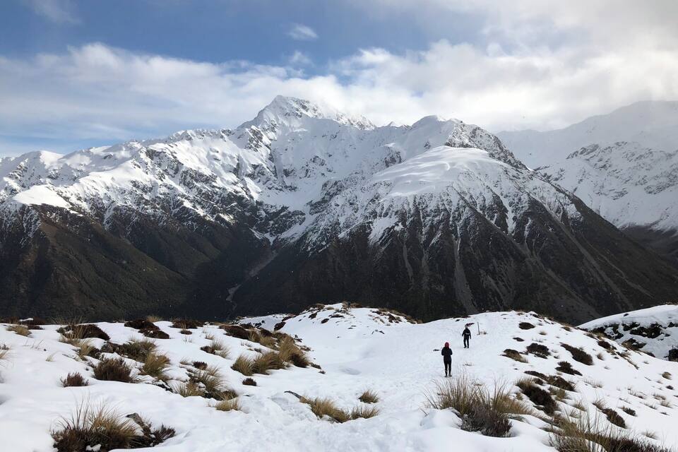 Cordilheira nevada com dois caminhantes em primeiro plano.