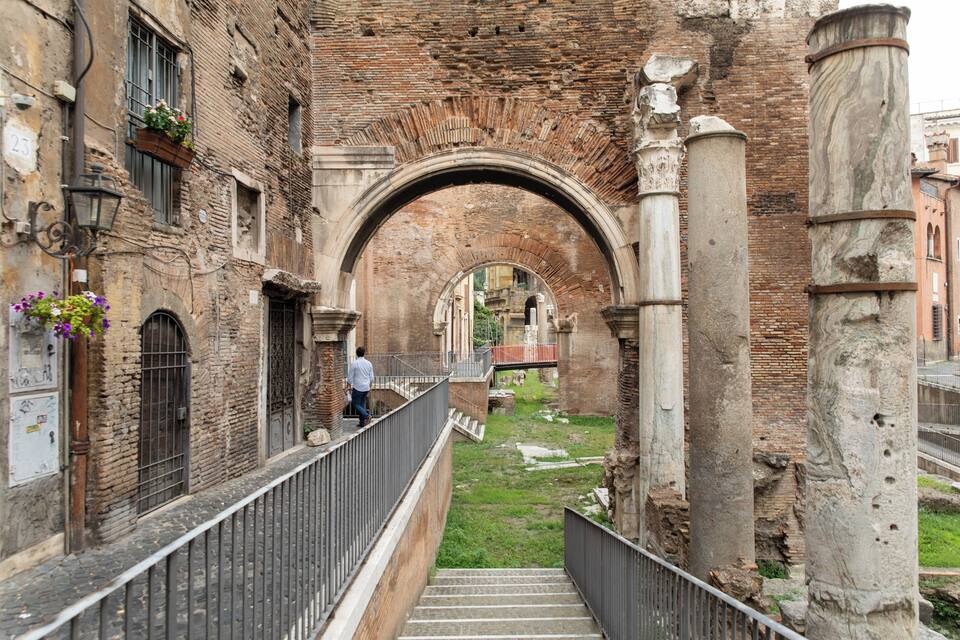 Un antiguo arco de piedra con barandilla de metal, que conduce a un patio cubierto de césped.