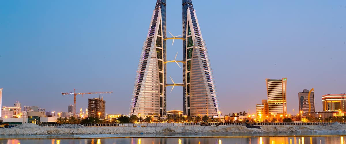 A modern architectural structure with two tall towers, a construction crane, and a waterfront.
