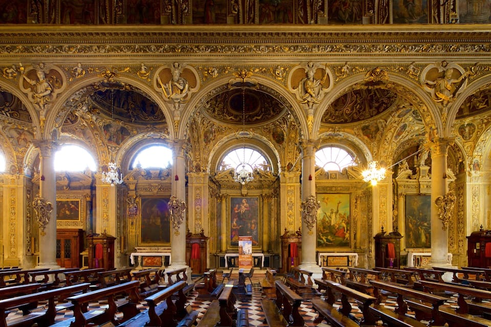 L’intérieur d’une église richement décorée, avec de hauts plafonds, des fresques détaillées et des rangées de bancs en bois.