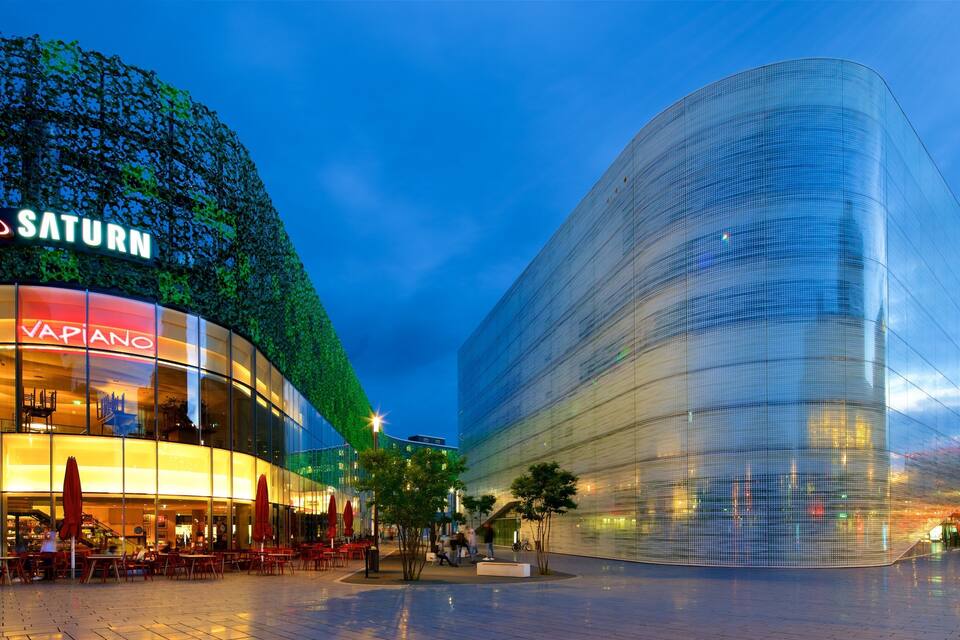 A modern building with a curved glass facade and a restaurant named "VAPIANO" with outdoor seating.