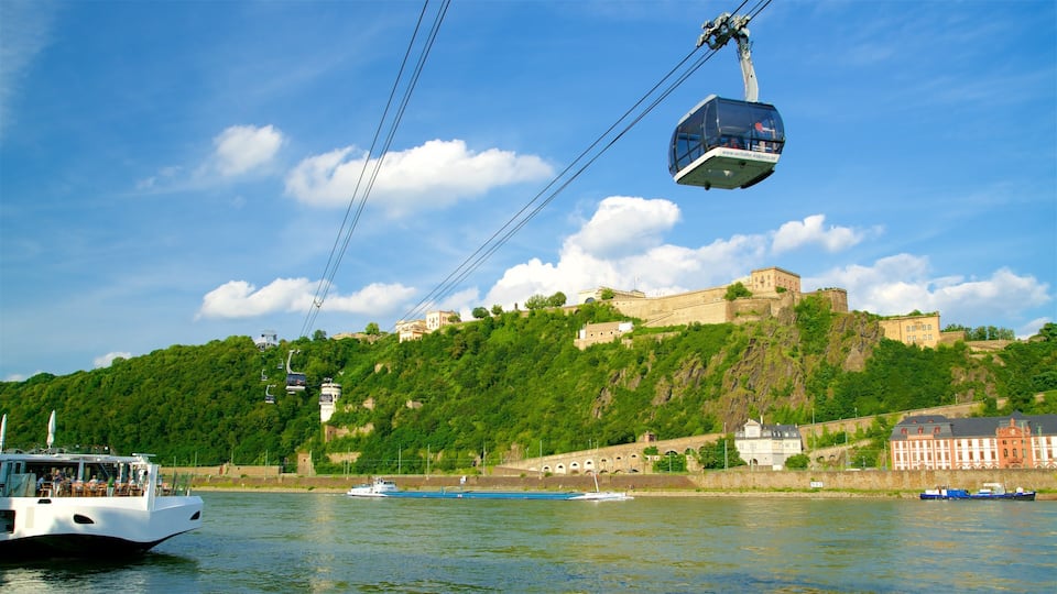 Eine Seilbahn über einem Fluss, eine Burg auf einem Hügel und Boote auf dem Wasser.