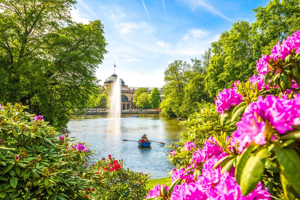 Een rivier met een fontein, omgeven door weelderig groen en felroze bloemen.