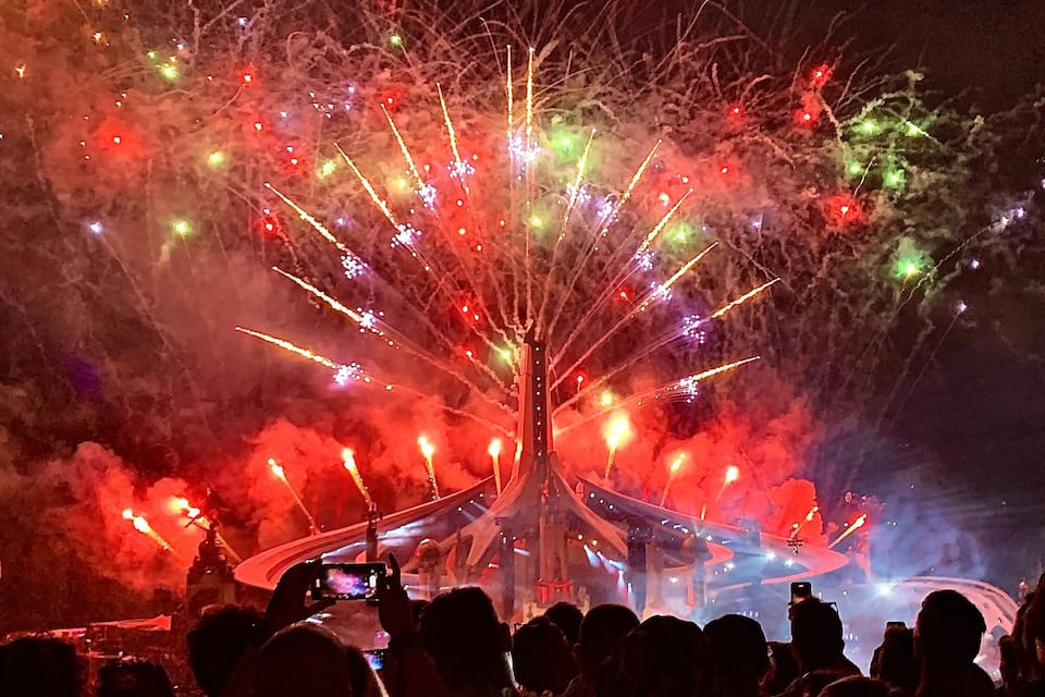 Espetáculo de fogos de artifício à noite, com uma estrutura central semelhante a uma árvore e efeitos de fumaça.