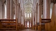 Ein Kircheninneres mit hohen Gewölbedecken, Holzbänken und farbigen Glasfenstern.