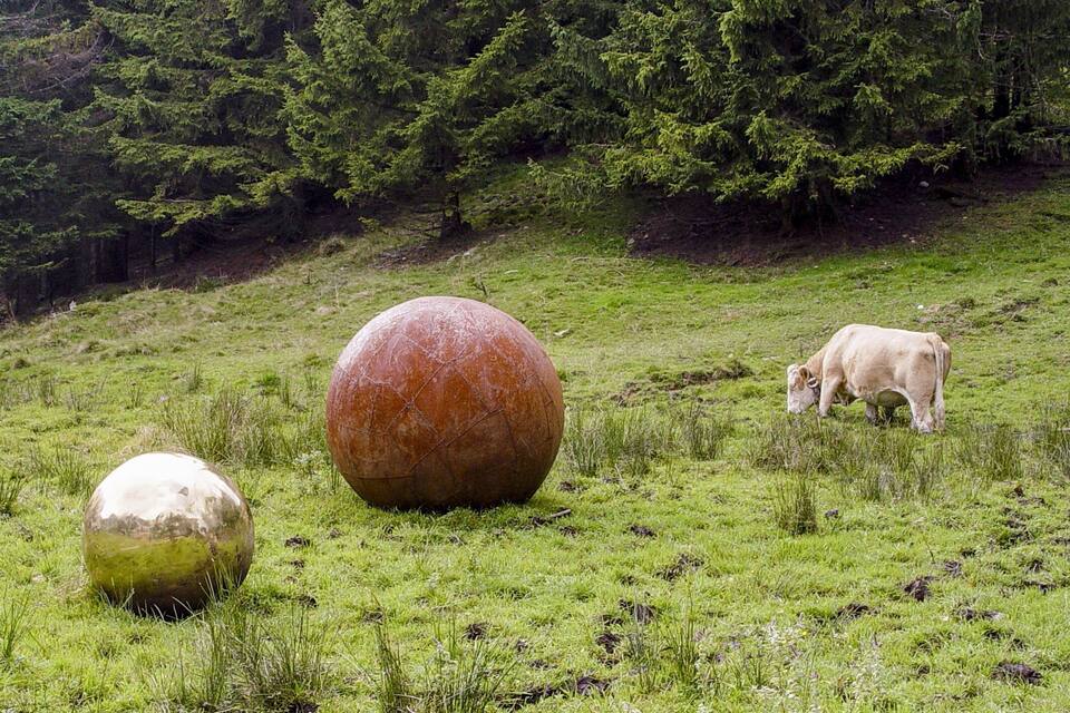 Un campo cubierto de césped con dos grandes esferas y una vaca pastando.