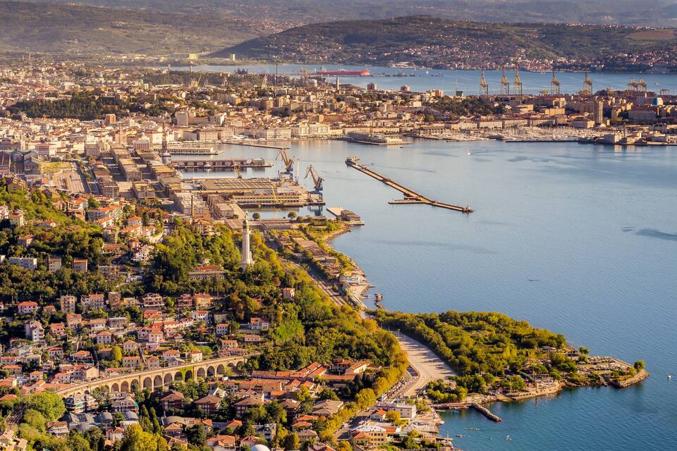 A coastal cityscape with a prominent bridge, industrial port, and residential areas.