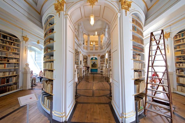Una maestosa biblioteca con architettura elaborata, alte scaffalature e una scalinata centrale.