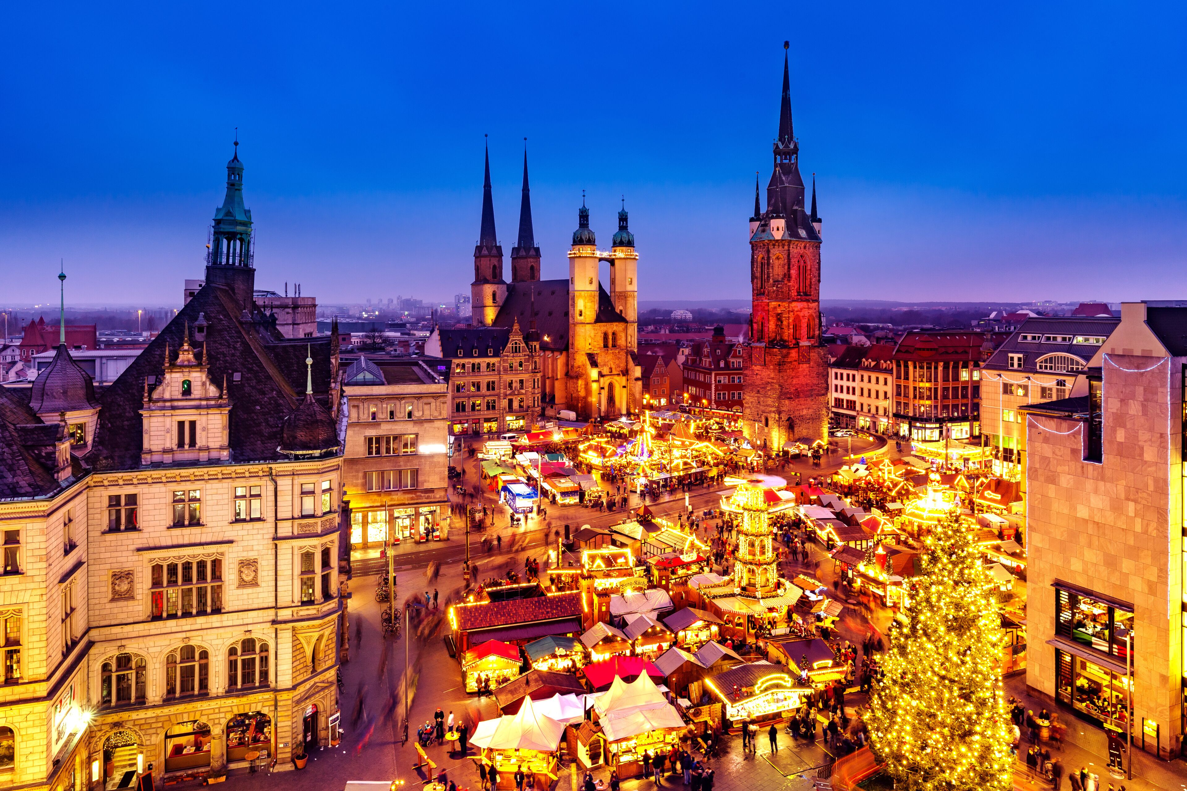 A historic city square with medieval architecture, including a prominent church with twin spires and a clock tower.