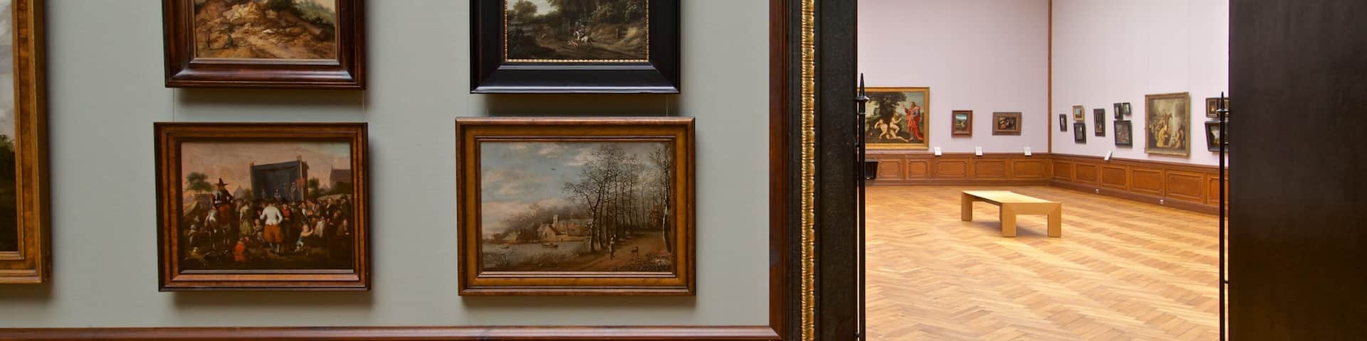 A gallery with framed paintings on the wall and a wooden bench in the center.