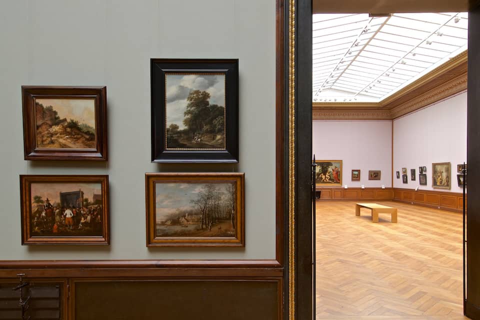 A gallery with framed paintings on the wall and a wooden bench in the center.