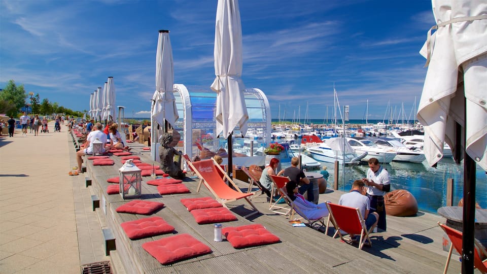 A marina with boats docked, people relaxing on deck chairs, and umbrellas providing shade.