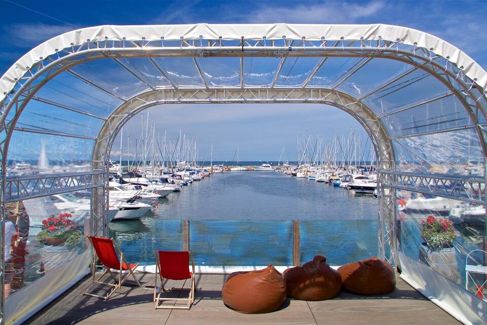 Eine transparente Markise blickt auf einen Yachthafen mit Booten und einem strahlend blauen Himmel.