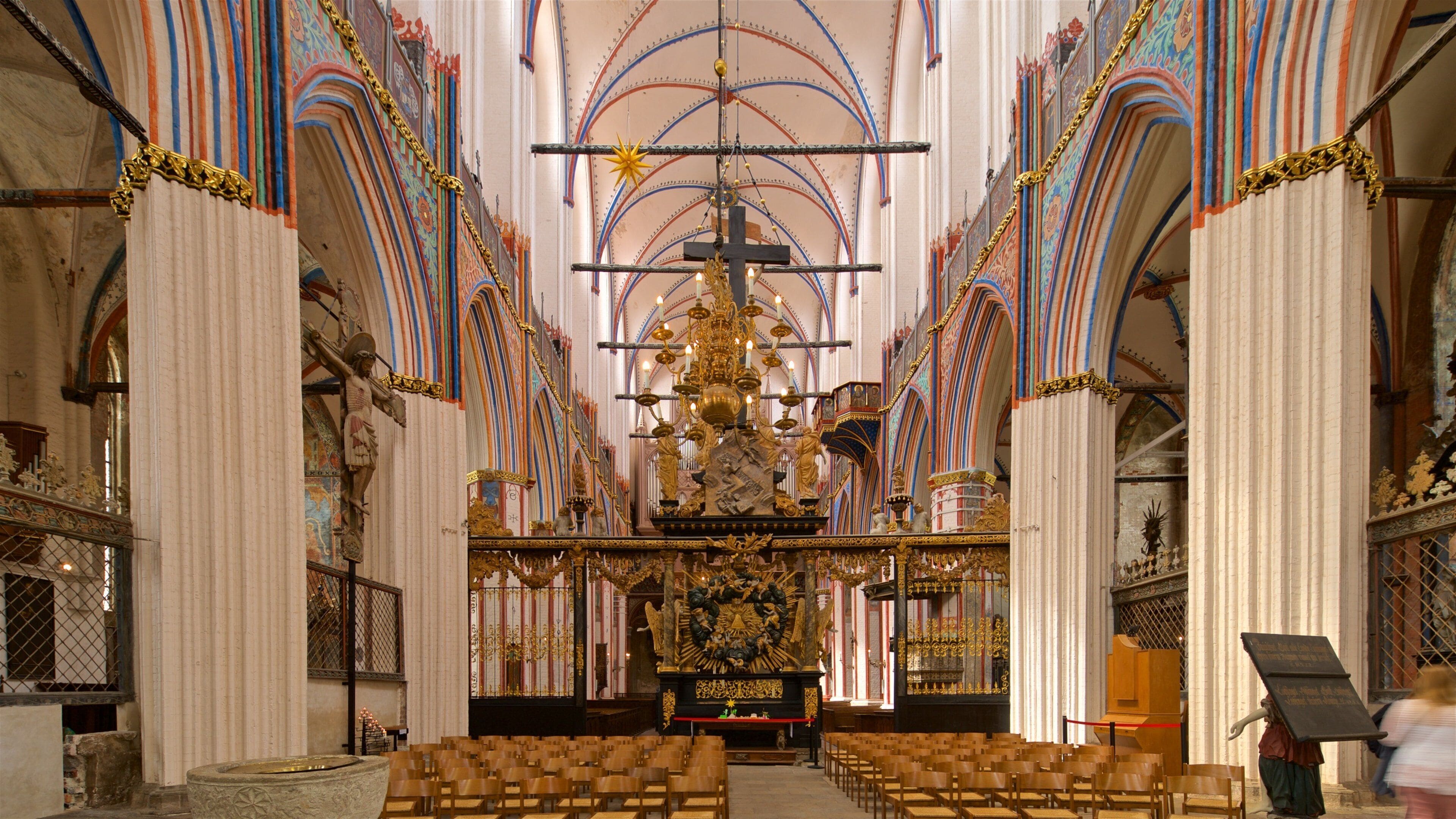 An ornate church interior with a central altar, rows of wooden pews, and intricate ceiling decorations.