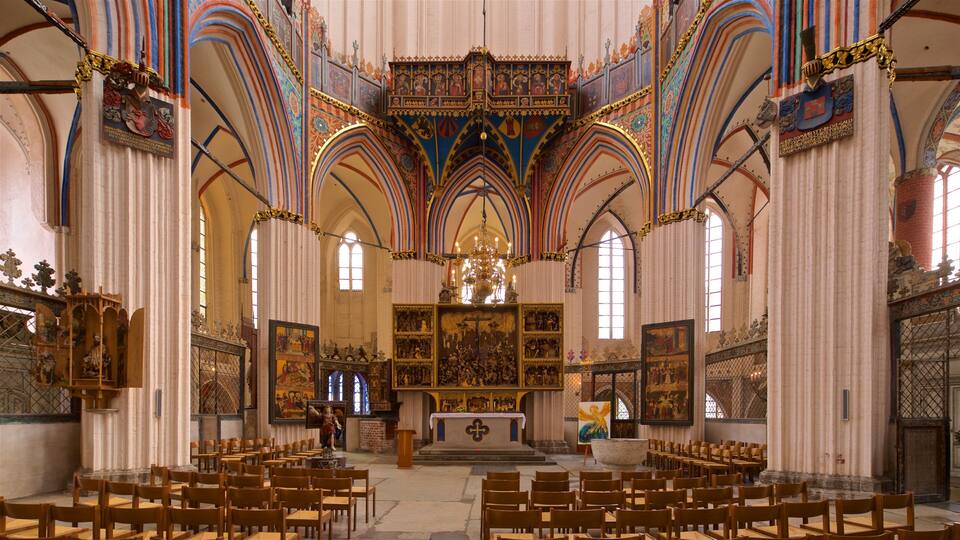 Interior de una iglesia ornamentada con altos techos abovedados, vidrieras y pinturas religiosas.