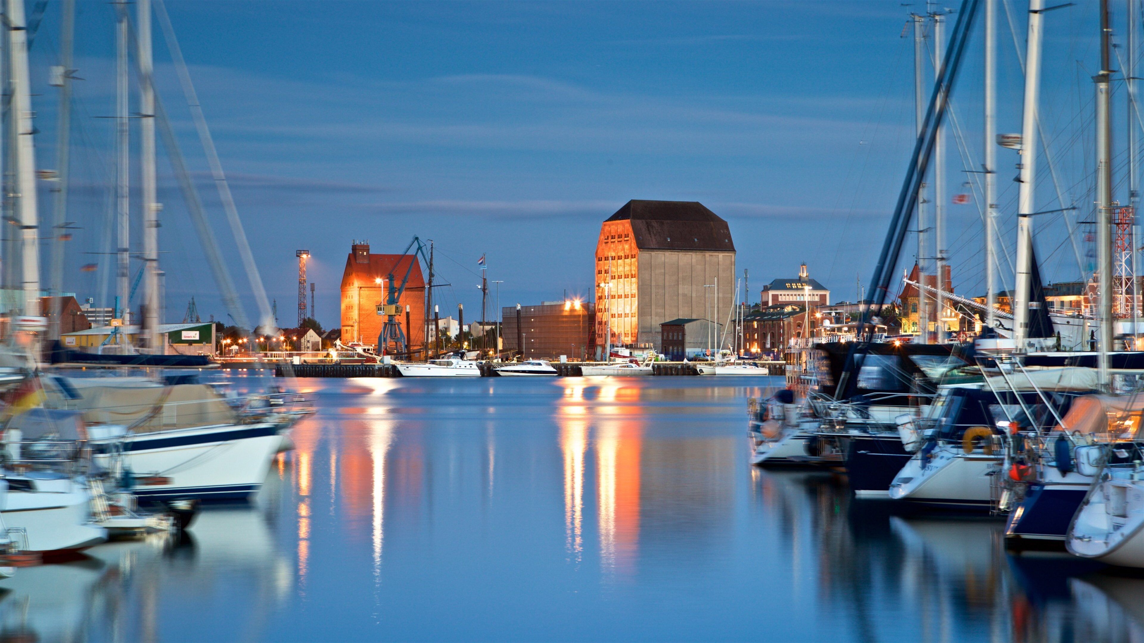 A marina with boats docked, a large building with a sloped roof, and a crane in the background.