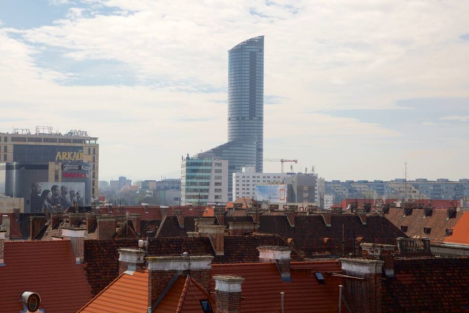 A cityscape with a prominent modern skyscraper, historic buildings, and red-tiled rooftops.